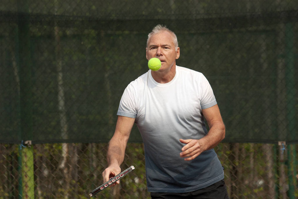 Мужчина играет в теннис на открытой площадке
 - Фото, изображение