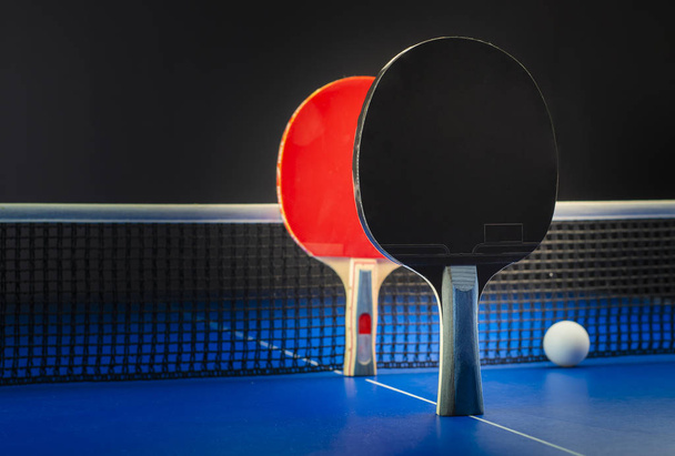 Raquetas y pelotas de ping pong sobre una mesa azul con red
. - Foto, Imagen