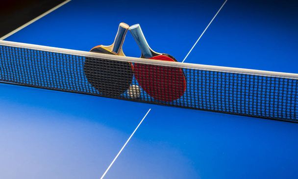 Racchette da ping pong e palline su un tavolo blu con rete
. - Foto, immagini