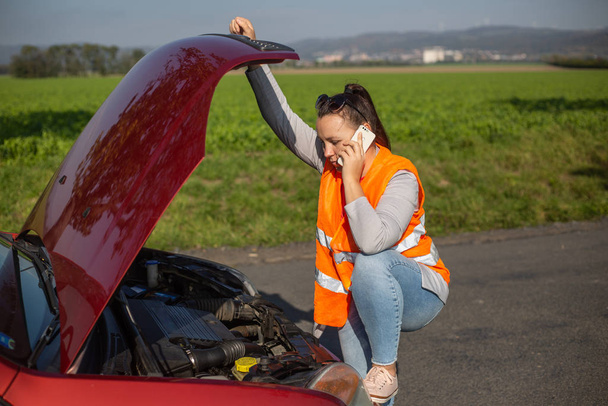 Раздраженная молодая женщина в ситуации дорожного бедствия - установка предупреждающего треугольника и призыв о помощи
 - Фото, изображение