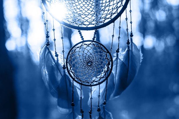 Dreamcatcher made of feathers, leather, beads, and ropes in classic blue trendy color of the year 2020. - Photo, Image