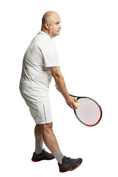 A bald man in adulthood in a white sports uniform with a tennis racket. Full height. Isolated over white background.  - Foto, afbeelding