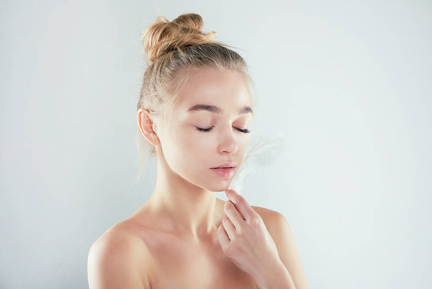 Portrait of attractive girl with closed eyes. beautiful woman with a white feather near her face. Face and body skin care concept, fresh clean shiny skin. - Valokuva, kuva