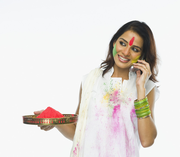 Woman holding Holi colors and talking on a mobile phone - 写真・画像