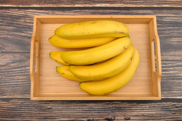 Bunch of ripe yellow bananas on a wooden tray on a wooden background. Close up. - Photo, Image