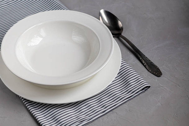 Eetinrichting. Prachtig serveren op een grijs linnen servet. Een bord voor soep of een bijgerecht. Lichtgrijze achtergrond en witte platen. - Foto, afbeelding