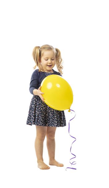 standing little girl holds a yellow balloon - 写真・画像