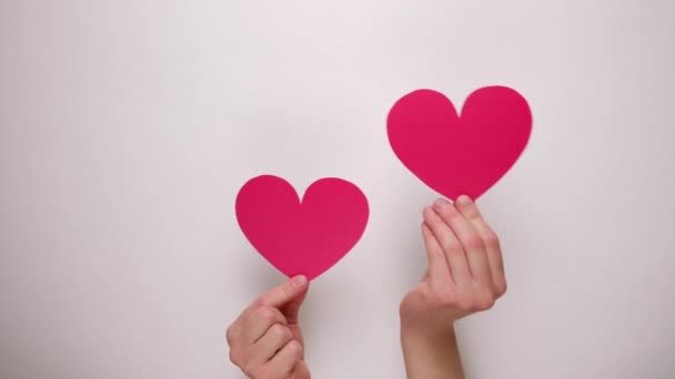 Acercamiento de manos femeninas sosteniendo corazones de papel rojo a través de una pared de papel blanco. Día de San Valentín y blog Me gusta blogging red social ternura concepto
. - Imágenes, Vídeo