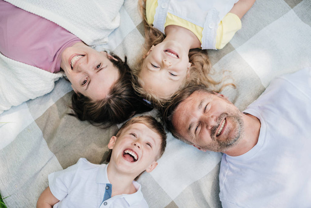 Family laying on the blanket looking at the camera. - 写真・画像