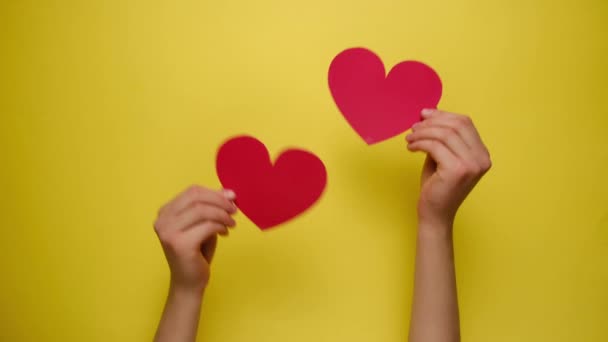 黄色い紙の壁を通して赤い紙の心を保持する女性の手の閉じる。バレンタインデーと母の日または人生の幸福の概念. - 映像、動画