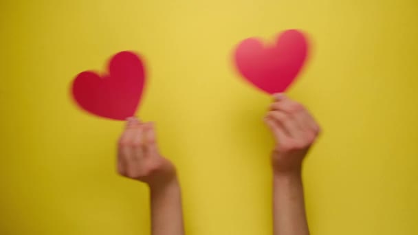 Fondo de vacaciones. Acercamiento de manos femeninas sosteniendo corazones de papel rojo a través de una pared de papel amarillo. Con lugar para el texto. Día de San Valentín, Día Internacional de la Mujer y concepto de cumpleaños
. - Metraje, vídeo