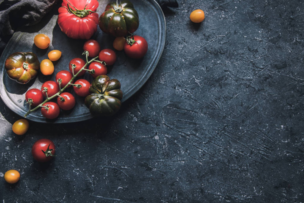 Ripe colorful different tomatoes on plate. Food background with copy space. - Foto, imagen