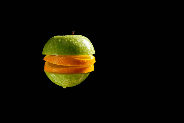 Pomme tranchée et orange avec des gouttelettes d'eau sur fond noir
 - Photo, image