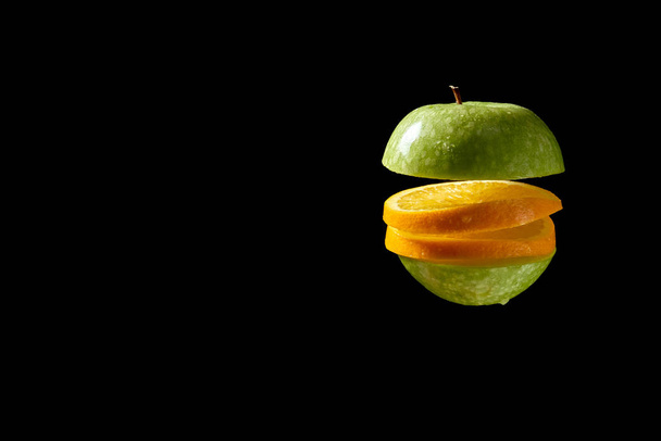 Pokrojone jabłko i pomarańcza z kroplami wody na czarnym tle - Zdjęcie, obraz