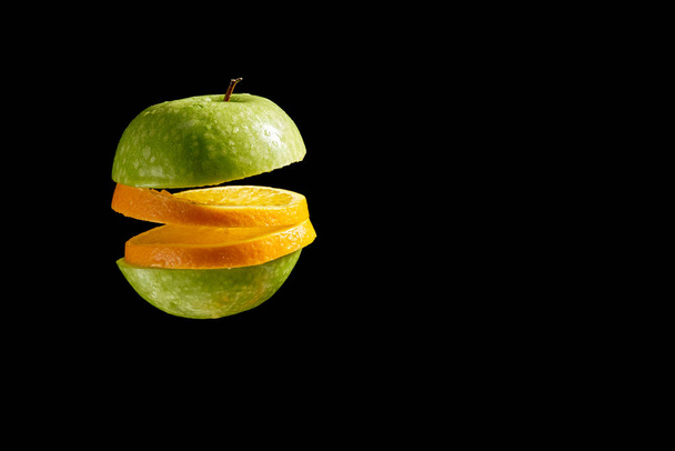 Κομμένο μήλο και πορτοκάλι με σταγονίδια νερού σε μαύρο φόντο - Φωτογραφία, εικόνα