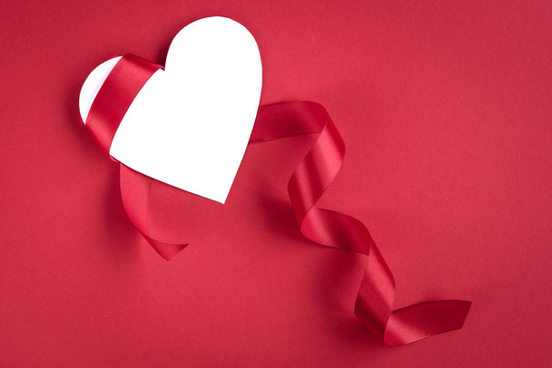 赤の背景に赤いサテンリボンとホワイトペーパーバレンタインカードハート。バレンタインデーのコンセプト - 写真・画像