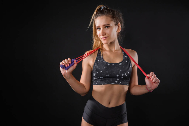 beautiful young woman in sportswear with a skipping rope in hands on a black background - Фото, зображення