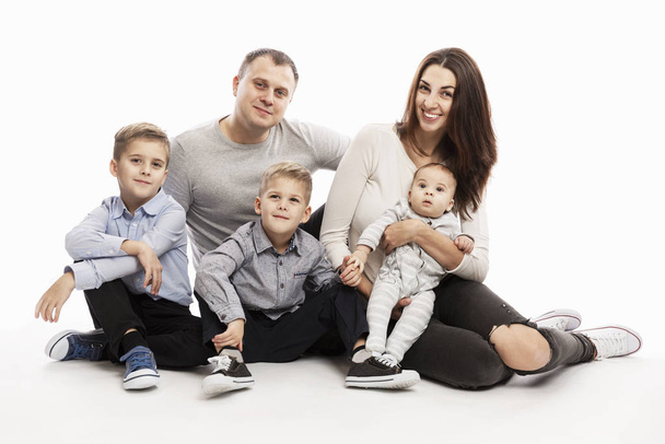 A young family with three children hugs and smiles while sitting. They look at the camera. Love and tenderness. White background. - Valokuva, kuva