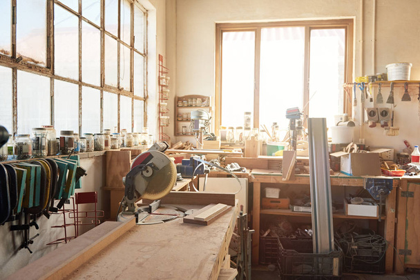 Interior of a large woodworking shop with a mitre saw and other tools and wood on workbenches, with flare in the background - Photo, image