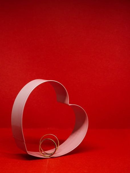 Каркас форми печива у формі серця. У центрі обручки. Червоний фон, ізольований, копіює простір для повідомлення. Концепція Дня Святого Валентина Декларація кохання
. - Фото, зображення