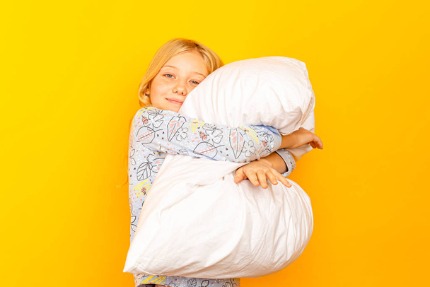Adorable niña mirando a la cámara y abrazando un fondo de almohada de una pared amarilla
 - Foto, imagen