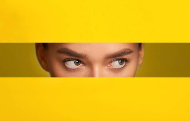 Dziewczęce oczy podglądające z otworu w żółtym papierze, panorama - Zdjęcie, obraz