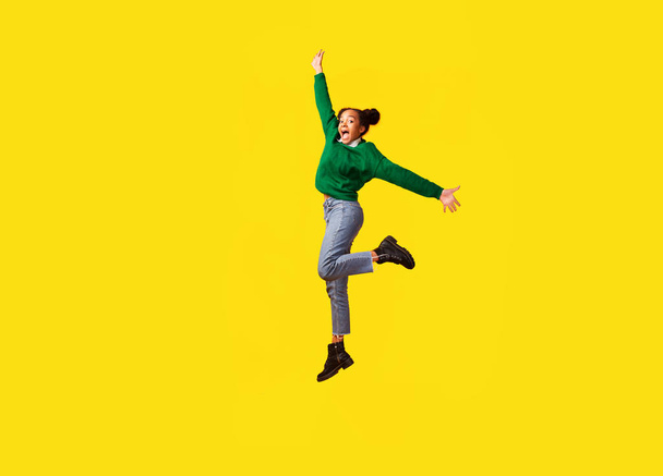 幸せなアフロ女の子ジャンプ上の黄色のスタジオの背景 - 写真・画像