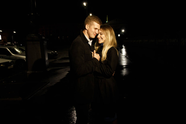 couple in love embracing against a dark background, night, rain, buildings in the city, a park, smiling, attraction. the guy hug the girl. Valentine's Day - Foto, afbeelding