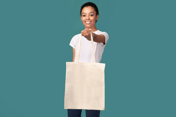 Chica mostrando blanco eco bolsa sonriendo de pie sobre fondo turquesa
 - Foto, imagen