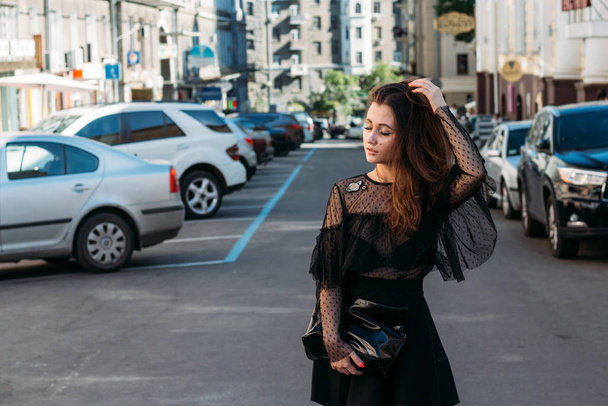 portrait of a girl, brunette, in a black dress, in the arch, in the city. posing, walking. alone in the crowd, loneliness - Foto, imagen
