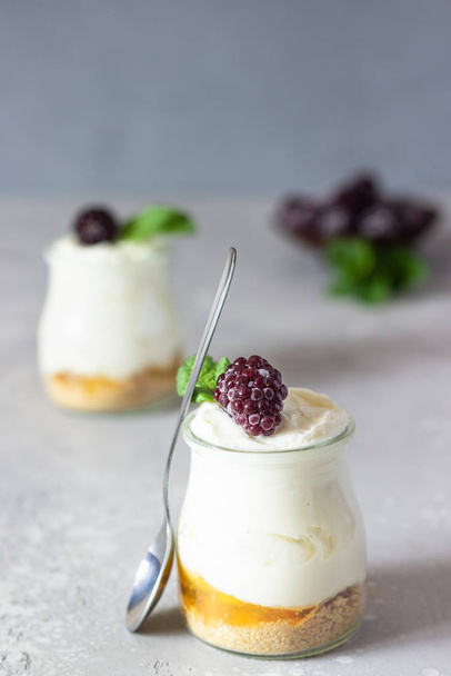 Homemade no baked dessert (cheesecake, trifle, mousse) with orange or peach jam in small portioned jars served with frozen berries and mint. Light grey stone background, copy space. - Valokuva, kuva