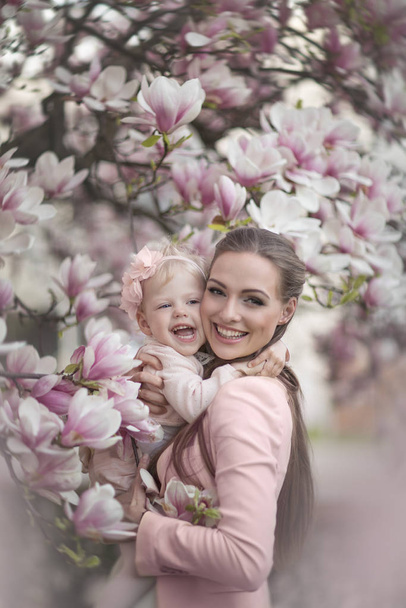 Piękna i szczęśliwa mama z córką w kwitnącej magnolii. - Zdjęcie, obraz