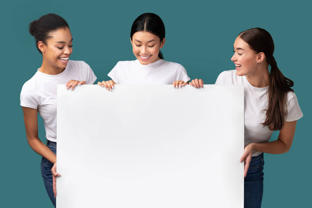 Tres niñas del milenio sosteniendo tablero blanco sobre fondo turquesa, burla
 - Foto, imagen