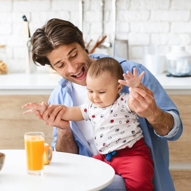 Cheerful daddy playing with curious baby son in kitchen - Foto, imagen