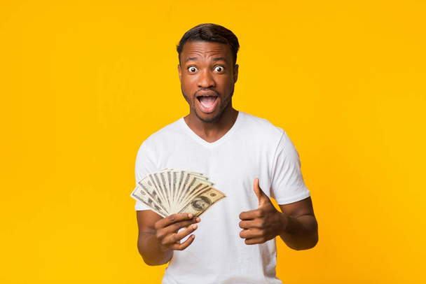 Shocked Afro Guy Holding Money Gesturing Thumbs Up In Studio - Fotó, kép