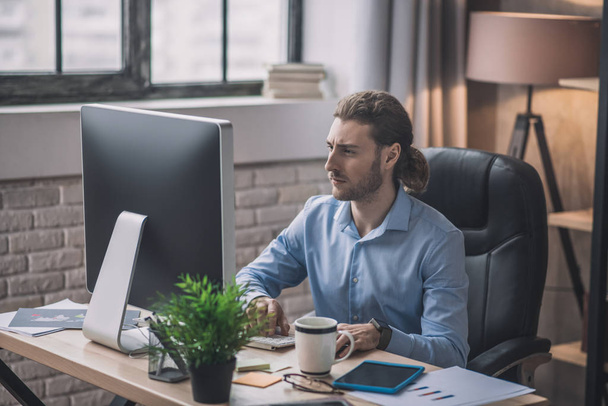 Young bearded man in blue shirt sitting in the office - Foto, Bild