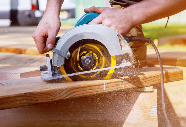 Ο κατασκευαστής πριονίζει μια σανίδα με κυκλικό πριόνι που κόβει μια ξύλινη σανίδα - Φωτογραφία, εικόνα
