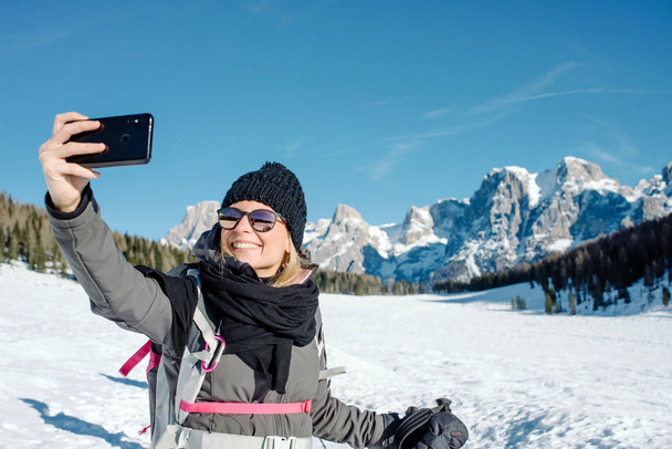 Молода мила дівчина взяла автопортрет з мобільним телефоном на снігу в сонячний день
 - Фото, зображення
