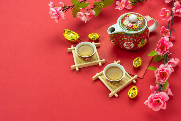 旧正月&中国の旧正月の休暇のコンセプトの背景のトップビュー。赤いポケットマネーと赤い紙の上にピンクの桜の花と紅茶のフラットレイカップ. - 写真・画像