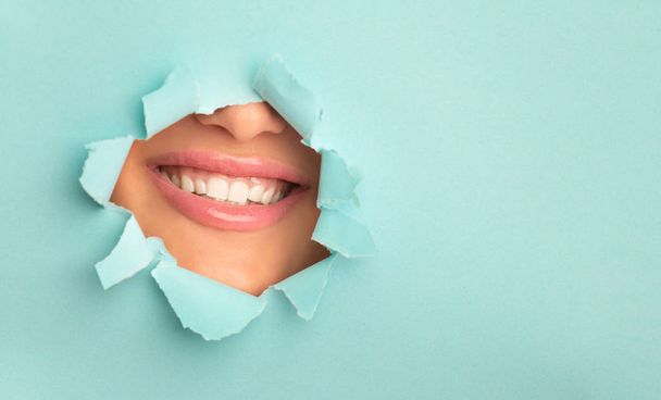 Donna con ampio sorriso, sbirciare attraverso carta strappata turchese
 - Foto, immagini