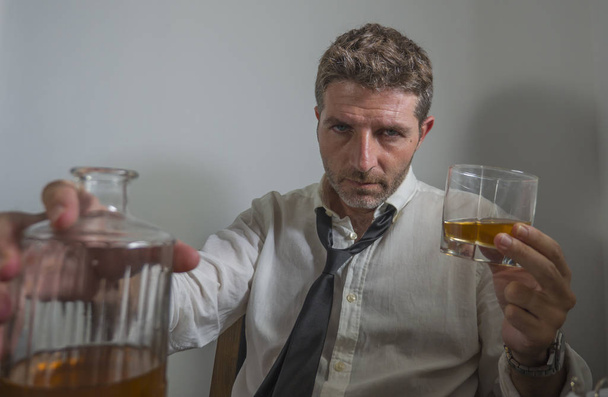 alcoholic  man in lose necktie drinking alcohol desperate and wasted looking at whiskey glass thoughtful drunk and depressed fighting his drinking addiction - Zdjęcie, obraz