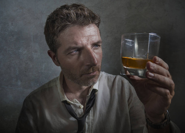 alcoholic  man in lose necktie drinking alcohol desperate and wasted looking at whiskey glass thoughtful drunk and depressed fighting his drinking addiction - Foto, Bild