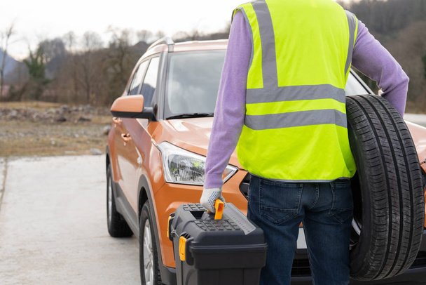 Photo of a mechanic dressed in high-visibility vest and ready to help, rear view. Professional emergency road service. RoadSide Assistance. - Photo, image