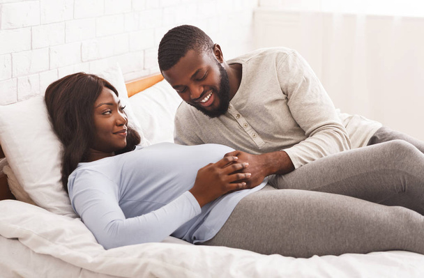 Happy young pregnant couple cuddling in bed at home - Foto, immagini