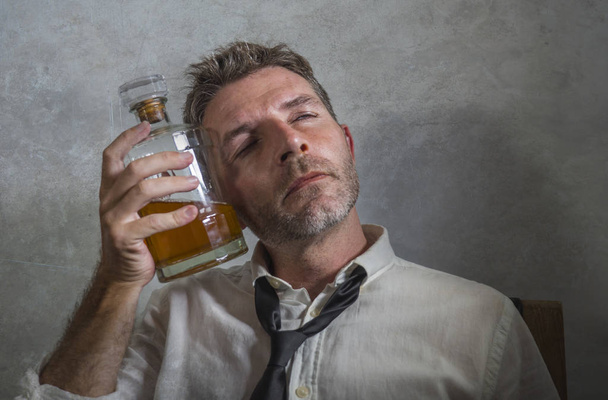 alcoholic man in lose necktie drinking alcohol desperate and wasted holding whiskey bottle feeling drunk and depressed drinking to evade reality in grunge edit - 写真・画像