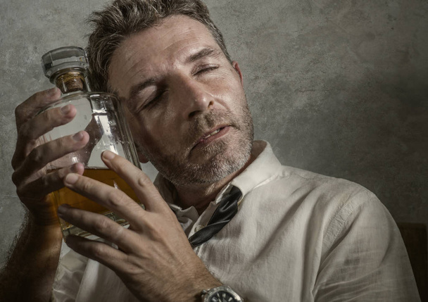 alcoholic man in lose necktie drinking alcohol desperate and wasted holding whiskey bottle feeling drunk and depressed drinking to evade reality in grunge edit - Foto, immagini