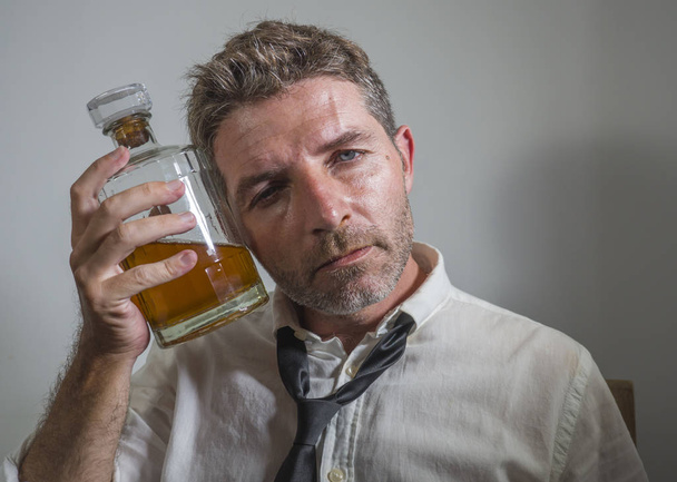 alcoholic man in lose necktie drinking alcohol desperate and wasted holding whiskey bottle feeling drunk and depressed drinking to evade reality in grunge edit - Photo, image