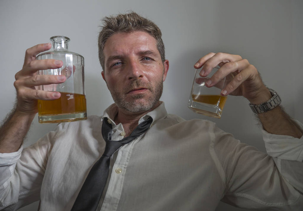 portrait of 30s to 40s alcoholic  man in lose necktie drinking desperate holding whiskey glass thoughtful drunk and depressed completely wasted in alcohol addiction concept - 写真・画像