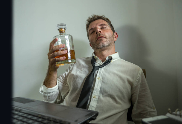 alcohol addict businessman - dramatic portrait of alcoholic  man in lose necktie drinking at office desk while working wasted and messy holding  whiskey bottle drunk and depressed - Foto, Bild