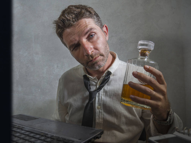 alcohol addict businessman - dramatic portrait of alcoholic  man in lose necktie drinking at office desk while working wasted and messy holding  whiskey bottle drunk and depressed - Foto, imagen